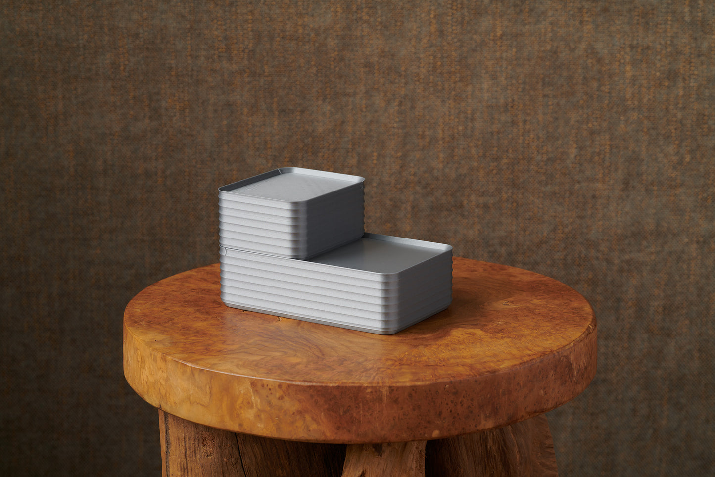Original size silver Rib Series Boxes styled arrangement photo in a stepped stack on a round wood stool with warm brown background, highlighting minimalist design.