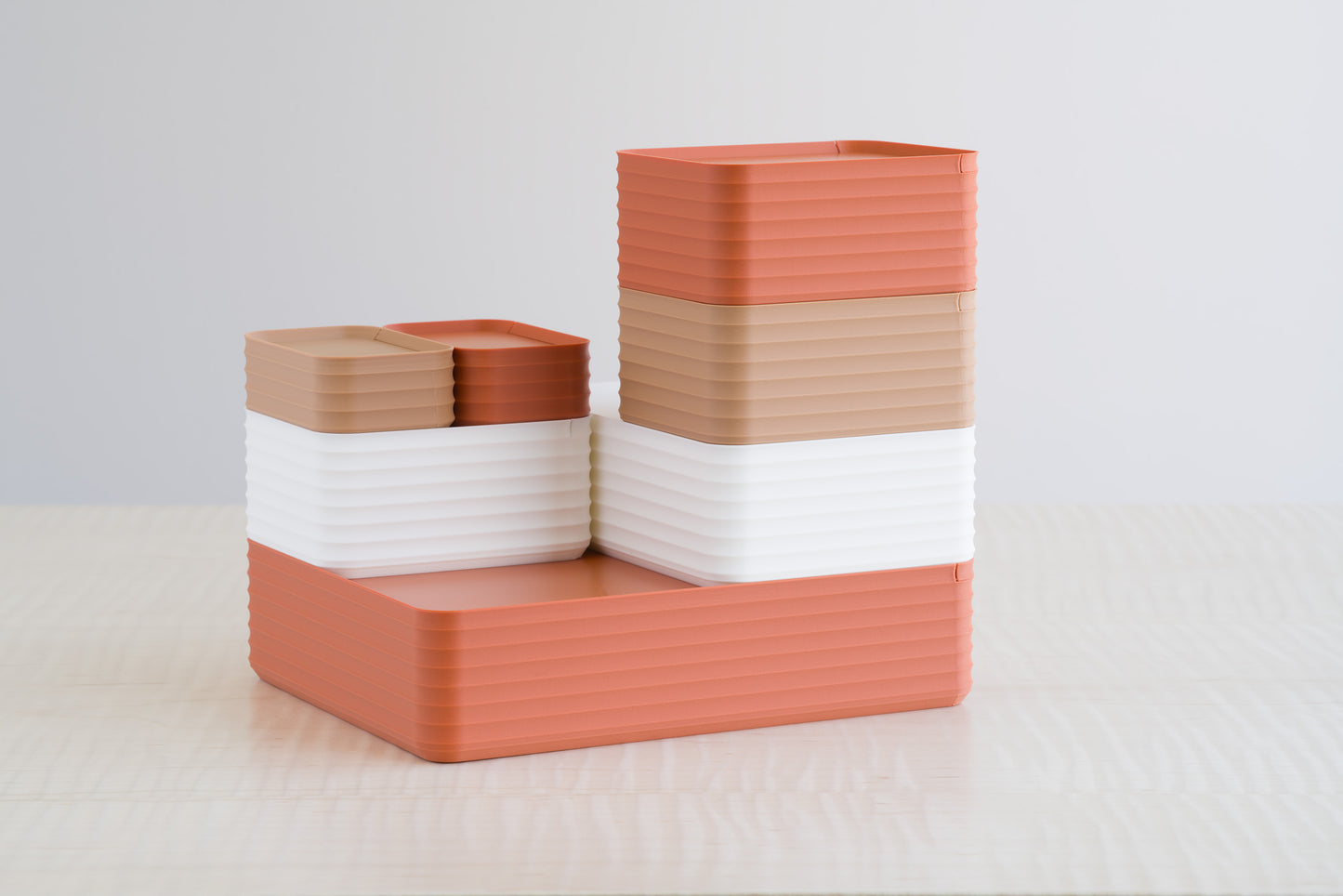 Stacked arrangement of Z Co Rib Series boxes in matte terracotta, caramel, and matte bone white. The earthy and neutral color palette is layered in horizontal bands, creating a warm, modern design accent on the maple tabletop.