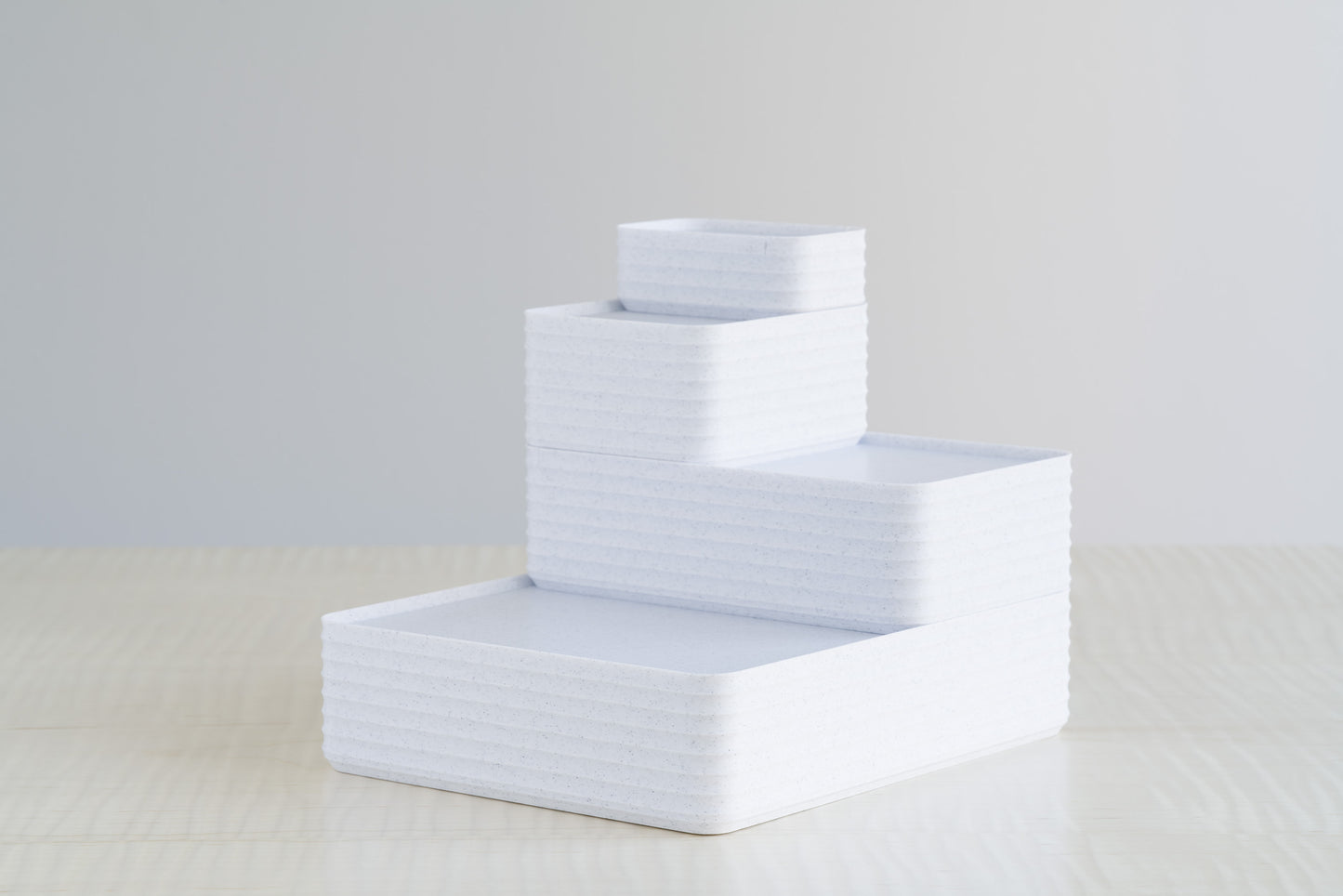 Four stacked ribbed boxes in marble white finish, arranged on a maple table for a clean minimalist storage display.