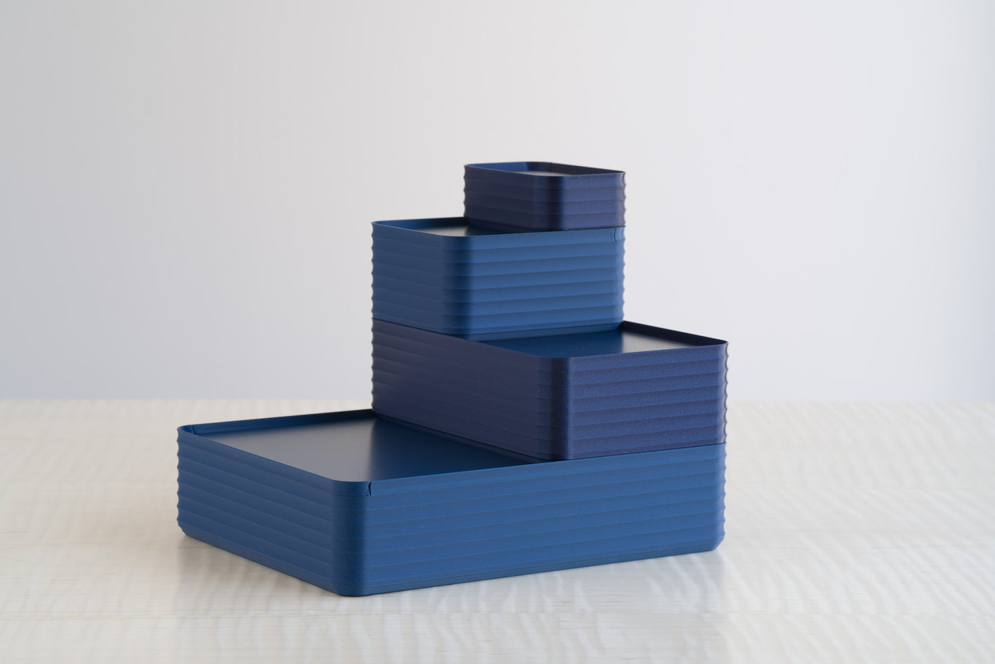 Side-by-side comparison of Z Co Rib Series boxes in matte dark blue and metallic deep blue, stacked in a tiered arrangement on a maple table to showcase the subtle difference in finishes.