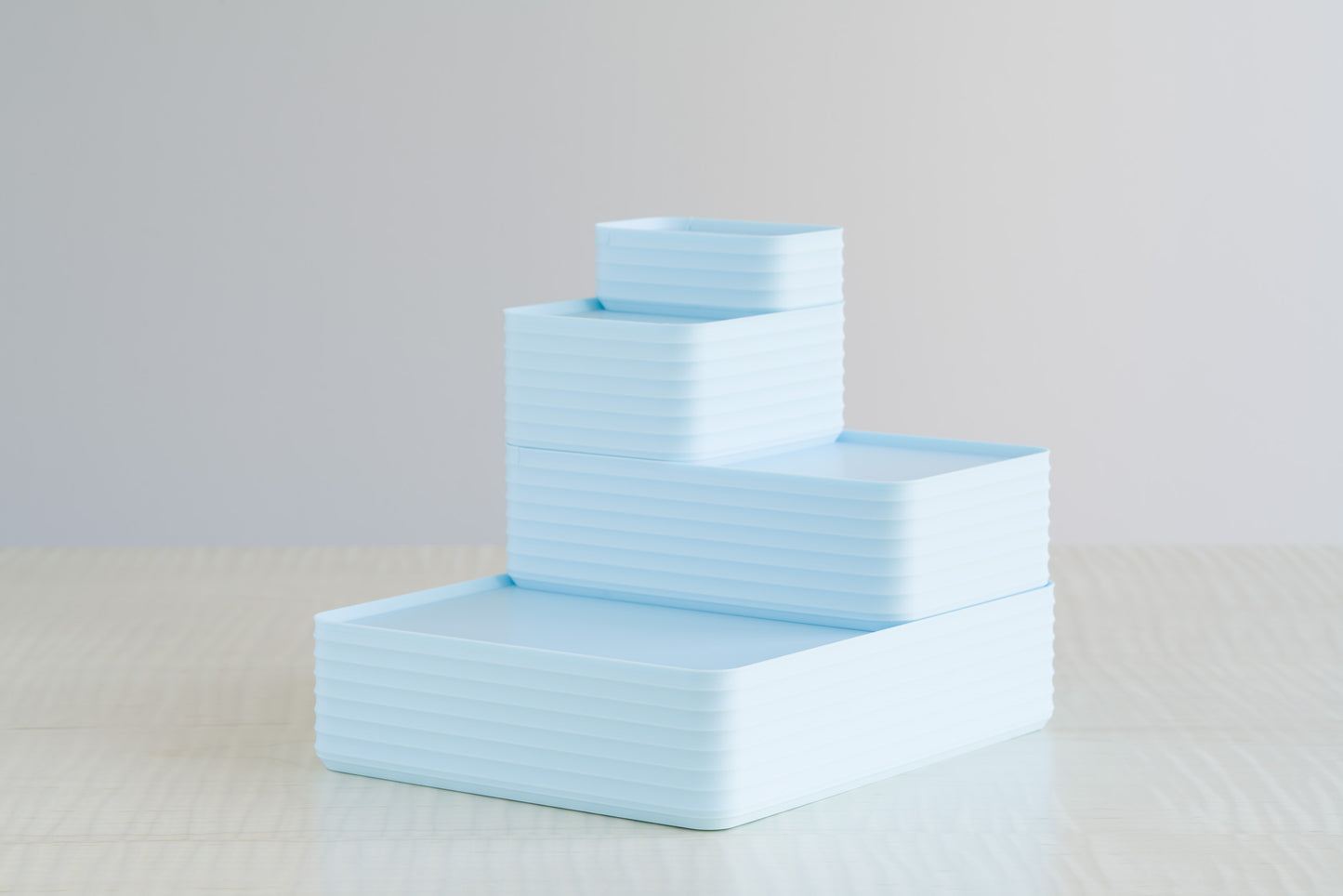 Four ribbed boxes in soft matte ice blue stacked neatly on a maple table, perfect as modern baby boy gift keepsake boxes or nursery storage décor.