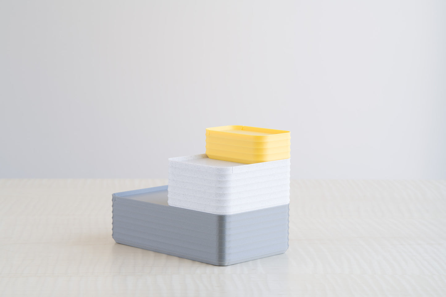 Stacked arrangement of Z Co Rib Series Boxes in Silver, Marble White, and Light Yellow, shown on a maple table with a clean minimalist background.