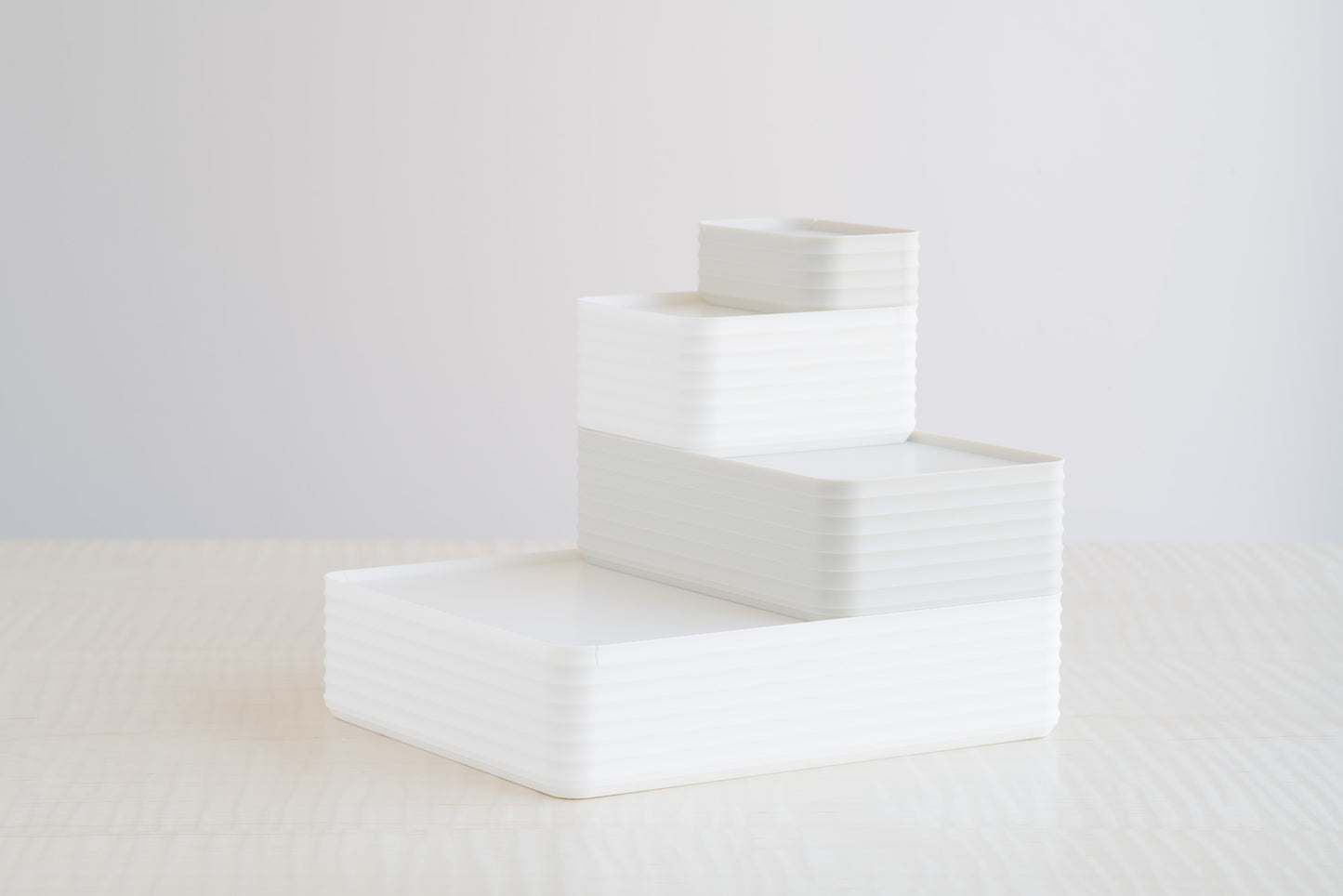 Two stacked ribbed boxes in white and matte bone white, styled on a maple table for a soft neutral modern storage arrangement.