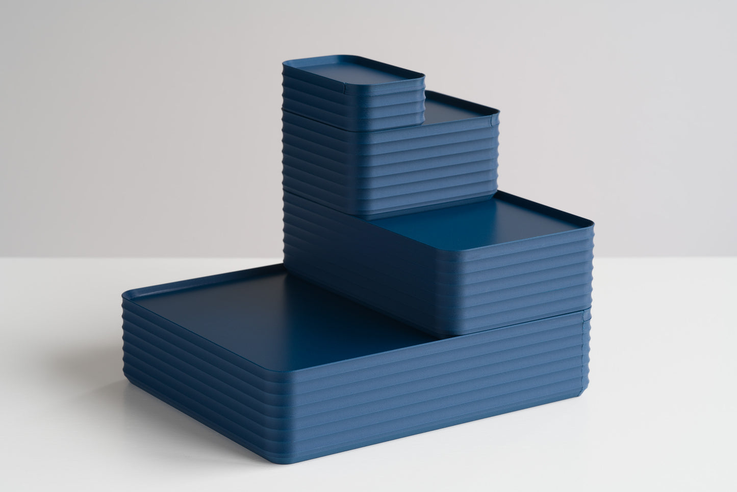 Four Z Co Rib Series Boxes in matte dark blue stacked on a white table. A stepped tower arrangement of all box sizes mini, small, original, and double-wide sizes with modern ribbed texture.