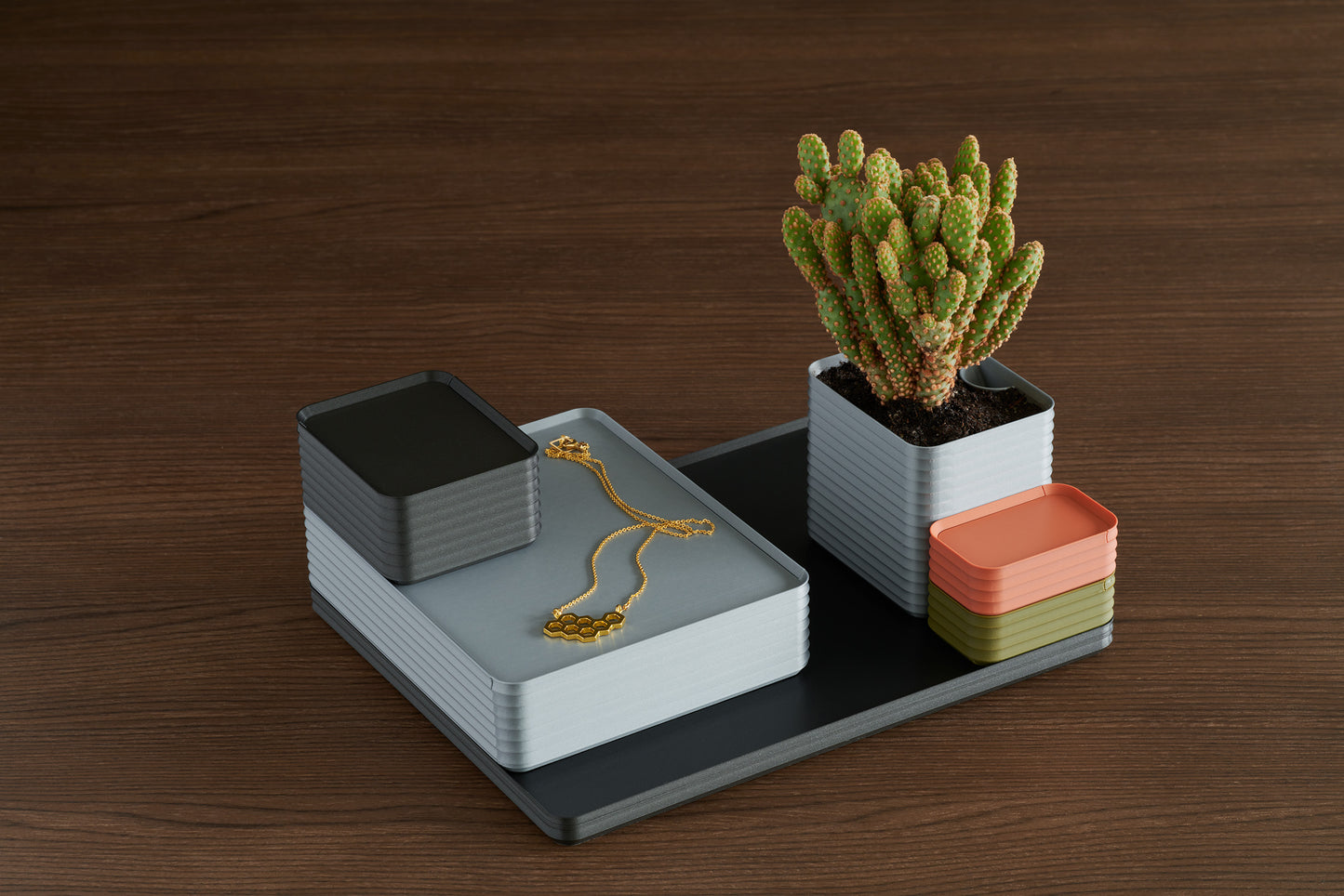 Arrangement of Z Co Rib Series Boxes including a double-wide silver box with necklace on top, iron gray box, matte terracotta and army green mini boxes, and silver planter with cactus, all placed on a black tray over walnut surface