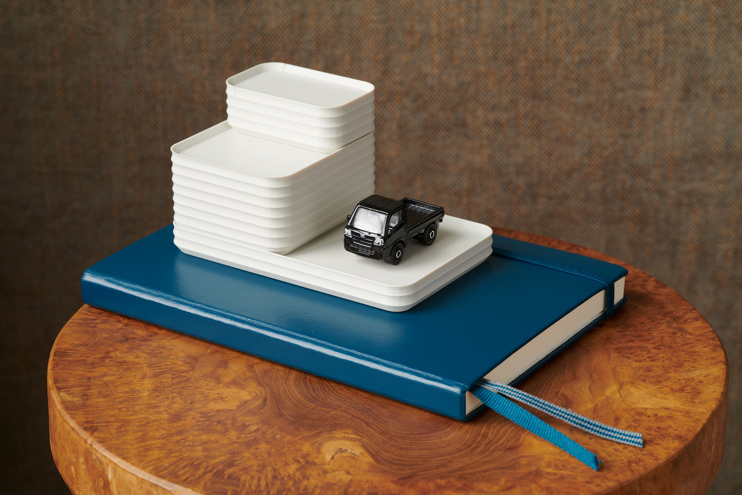 Z Co Rib Series arrangement in bone white stacked on a blue notebook with a miniature black toy truck. Displayed on a round wood stool, this playful styling emphasizes creative arrangements and makes a thoughtful inspiration for Z Co Gift Card gifting.