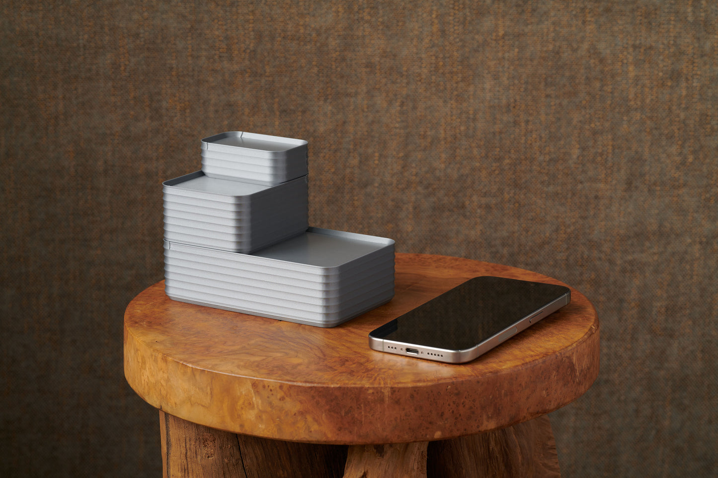Original size silver Rib Series Boxes stacked on a wood stool beside a smartphone, showing modern storage design and scale reference.