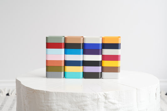 Stacked display of Z Co mini boxes in assorted colors on white stool with neutral background