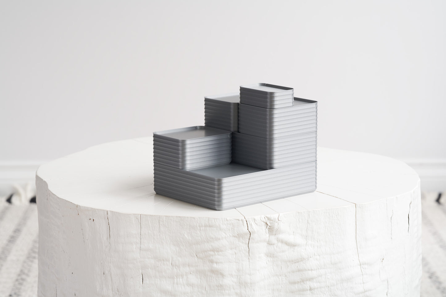 Arrangement of six silver Z Co boxes stacked on white stool with neutral background
