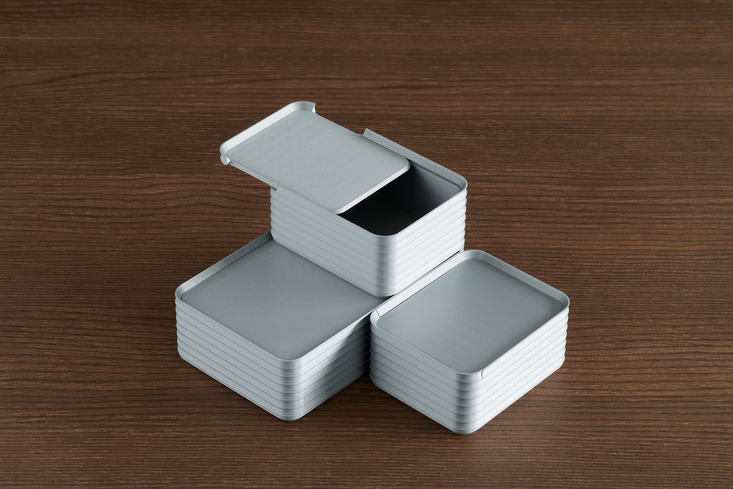 Arrangement of three silver Z Co ribbed boxes on a walnut table, with one box stacked on top and its sliding lid partially open to showcase interior space and modular design.