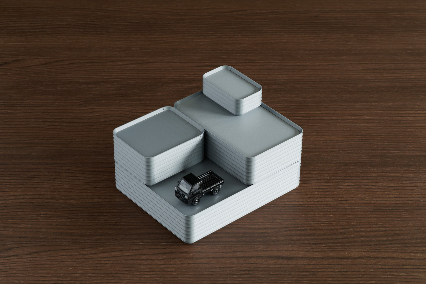 Arrangement of four stacked silver Z Co ribbed boxes in varying sizes, placed on a walnut surface with a small black toy truck positioned on top of the largest box.