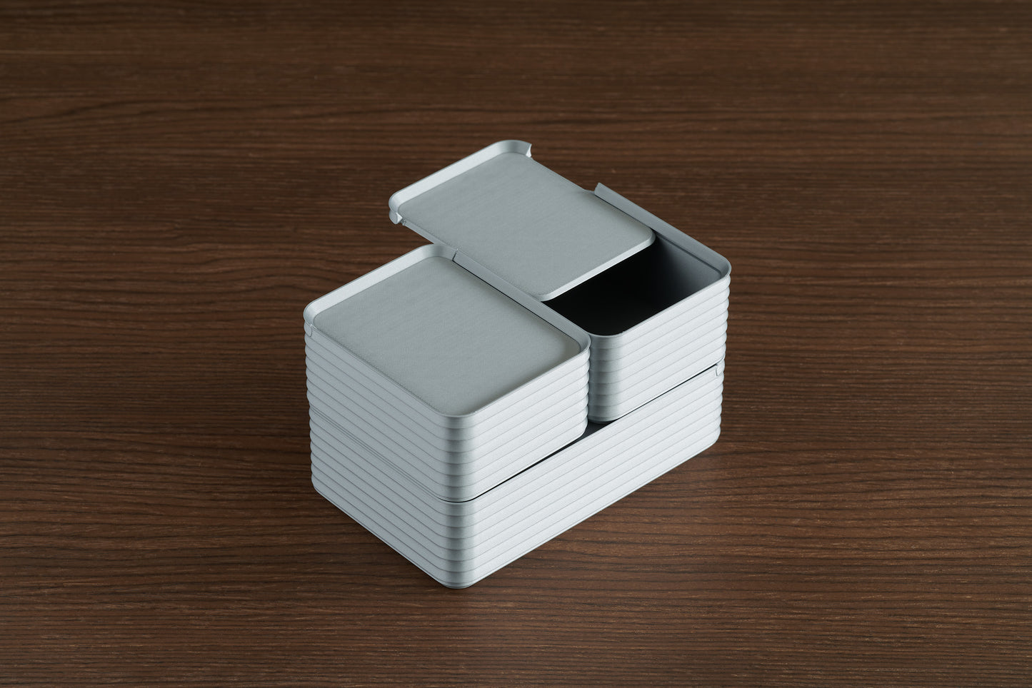 Arrangement of stacked silver Z Co ribbed boxes on a walnut surface, with the back small box open to reveal its sliding lid function.