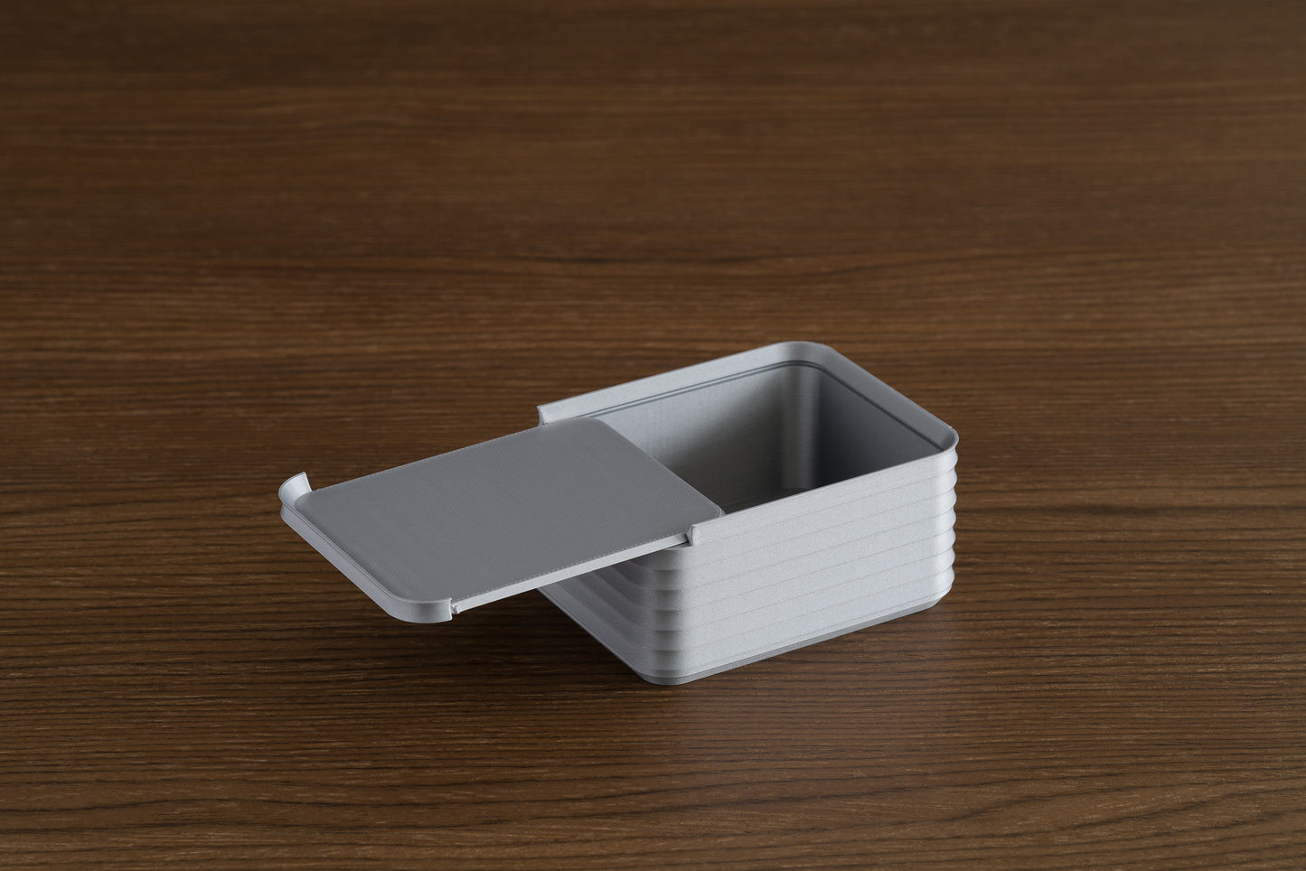 Small silver Z Co box on a walnut surface with its sliding lid partially open, showing the ribbed sides and interior.