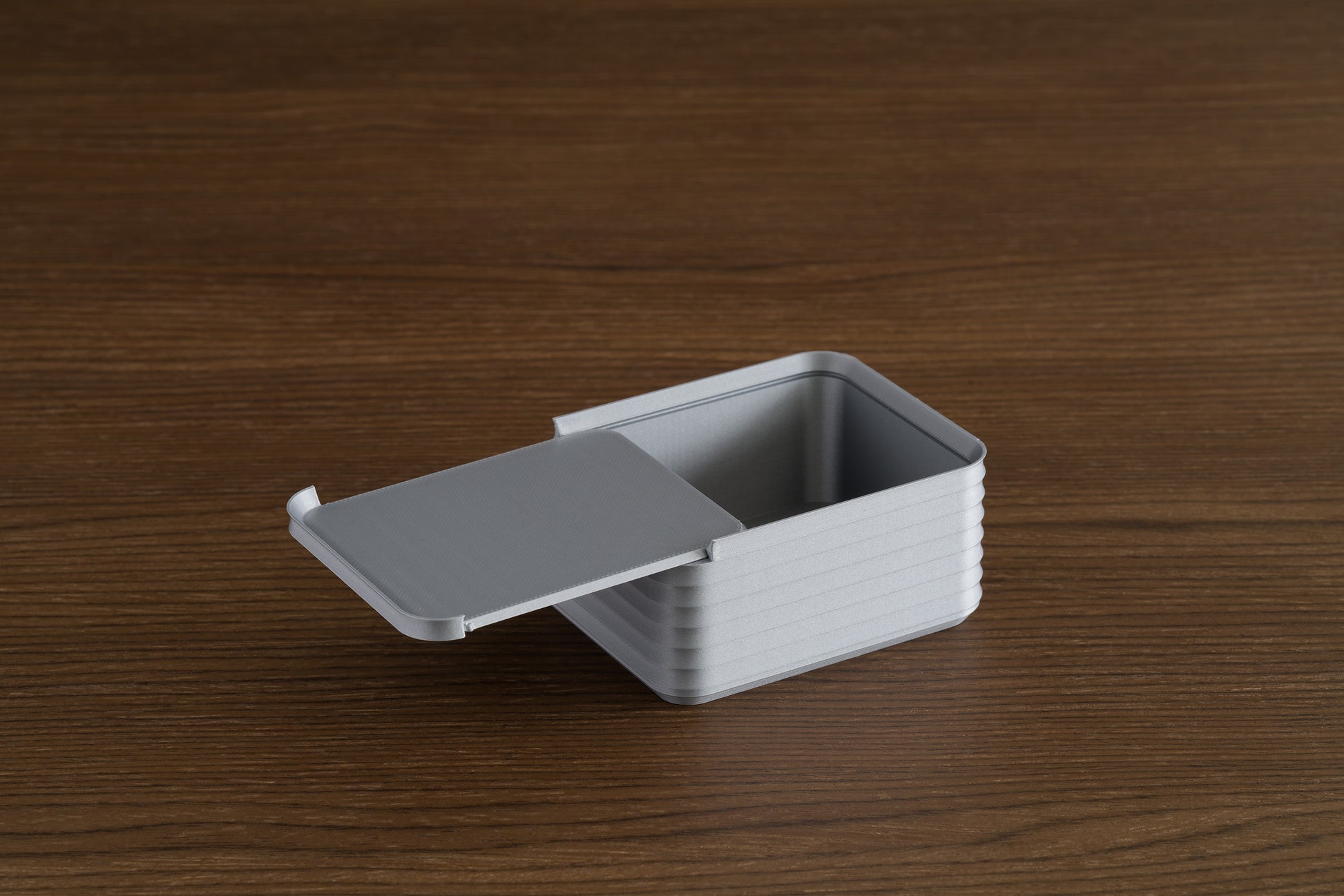 Small silver Z Co box on a walnut surface with its sliding lid partially open, showing the ribbed sides and interior.