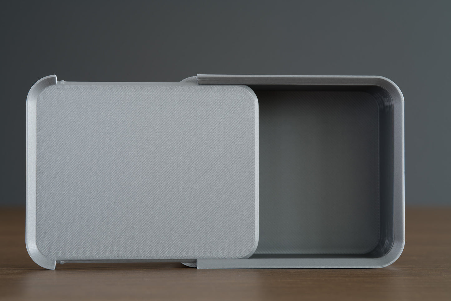 Small silver Z Co box resting on its side on a walnut surface, with the lid slid open to reveal the interior.