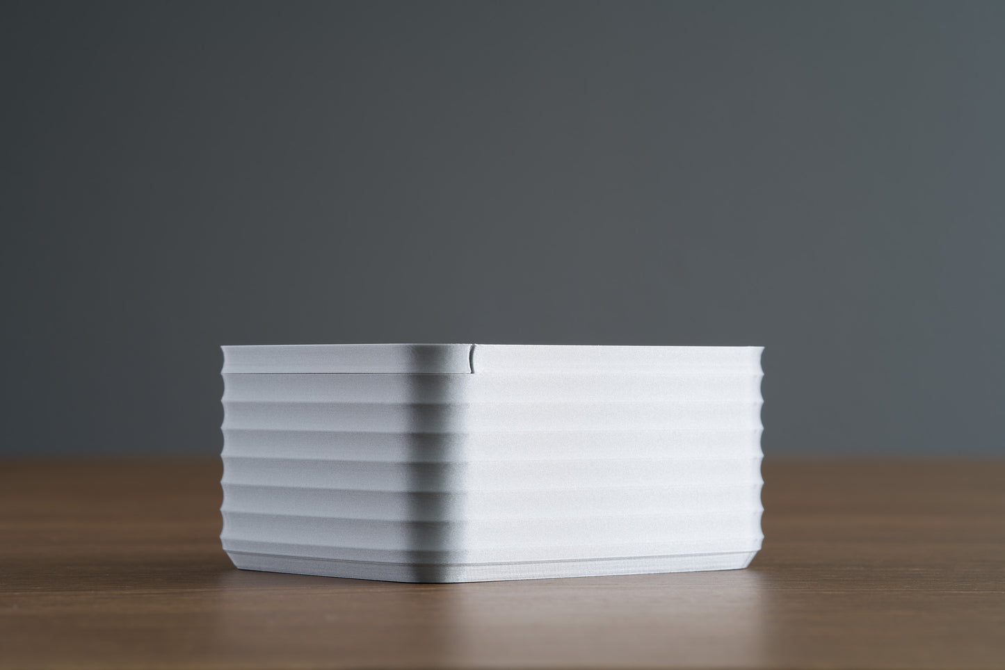 Small Silver Z Co ribbed box side view showing lid seam, placed on walnut surface with dark background.