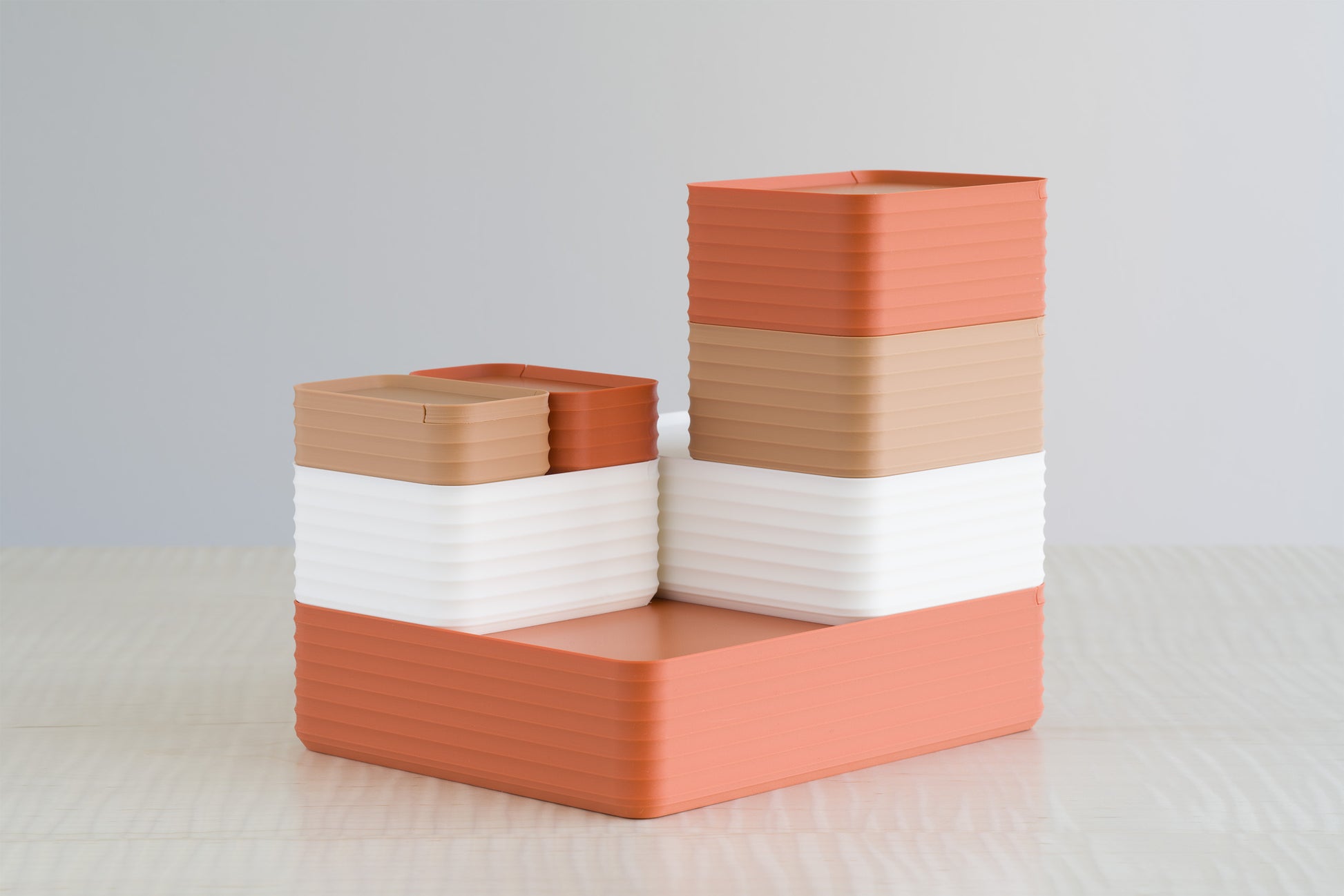 Stack of ribbed storage boxes in bone white, terracotta, and caramel brown on a maple table, showing warm autumn earthy color tones.
