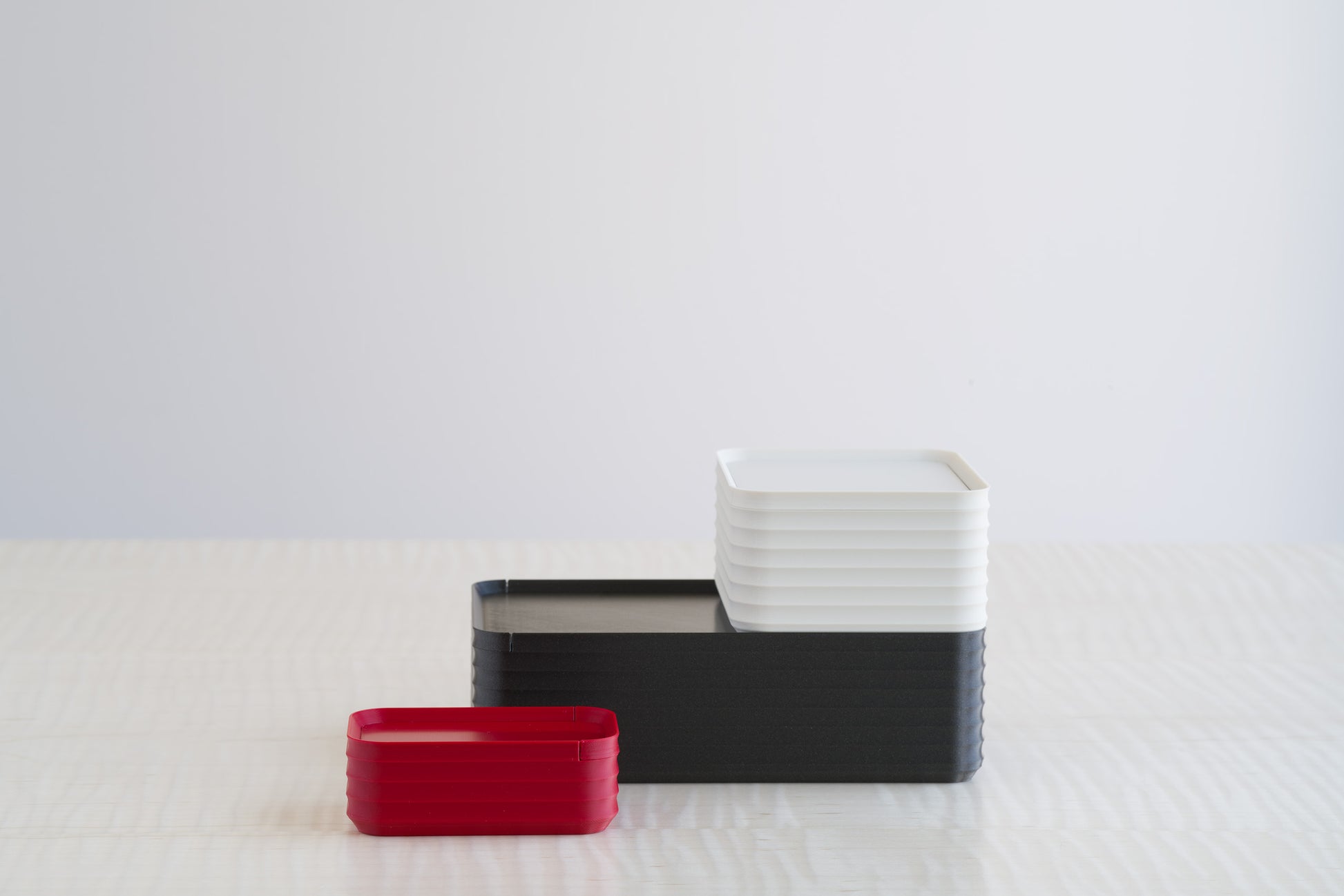 Minimalist arrangement of Z Co Rib Series boxes in crimson red, metallic iron gray, and bone white on a maple table, contrasting modern neutrals with a pop of vibrant color.