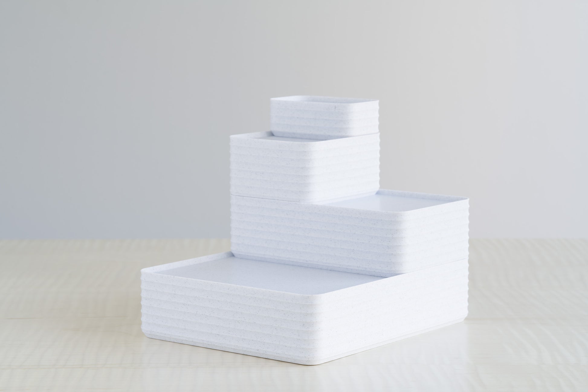 Four stacked ribbed boxes in marble white finish, arranged on a maple table for a clean minimalist storage display.