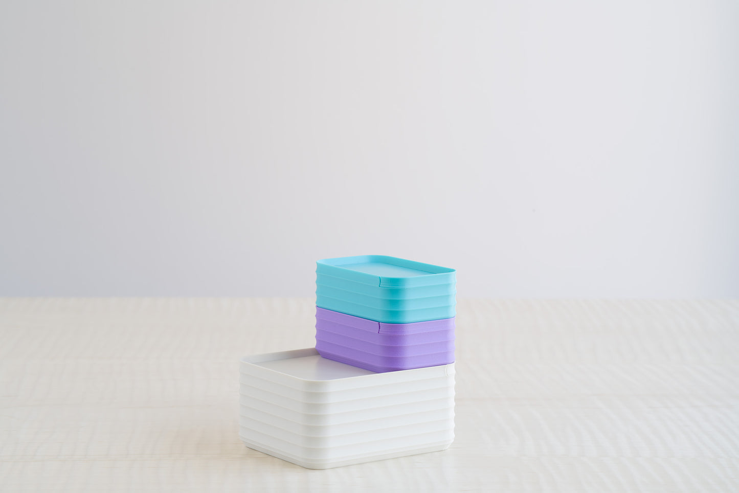 Playful arrangement of Z Co Rib Series Boxes in Bone White, Turquoise, and Lilac colors, stacked together on a light maple table.