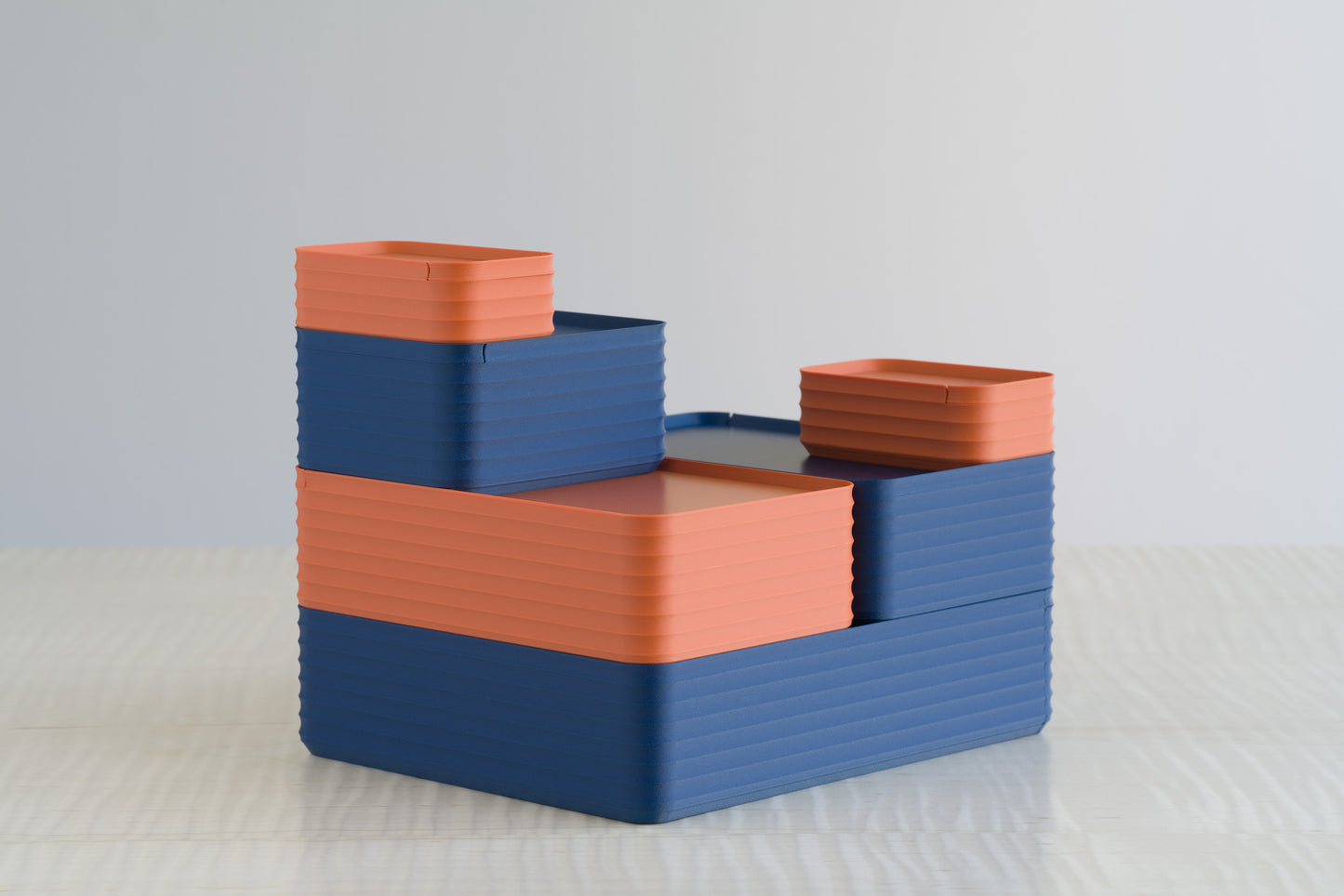 Tiered arrangement of Z Co Rib Series boxes in matte terracotta and matte dark blue on a maple table, showcasing the modern balance of warm and cool tones.