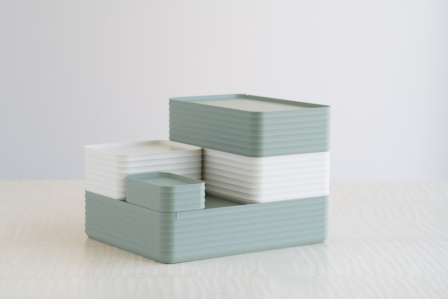 Z Co Rib Series boxes in matte tranquil green and matte bone white arranged together in a tiered formation on a maple table, highlighting the soft, earthy tones of this color pairing.