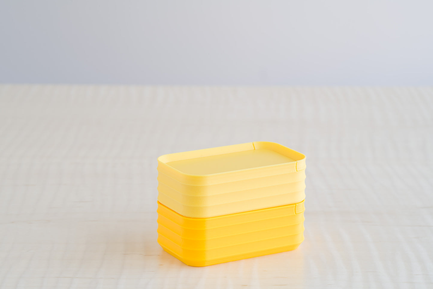 Rib Series Mini Boxes in matte light yellow and sunflower yellow, stacked on a light wood table, showing a bright and cheerful yellow palette.