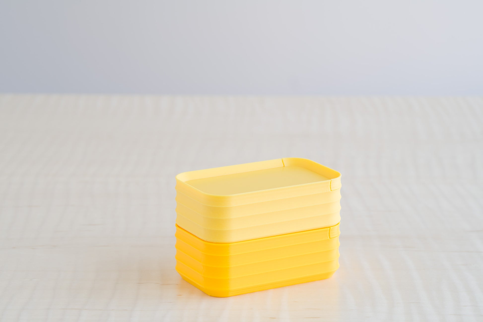 Rib Series Mini Boxes in matte light yellow and sunflower yellow, stacked on a light wood table, showing a bright and cheerful yellow palette.