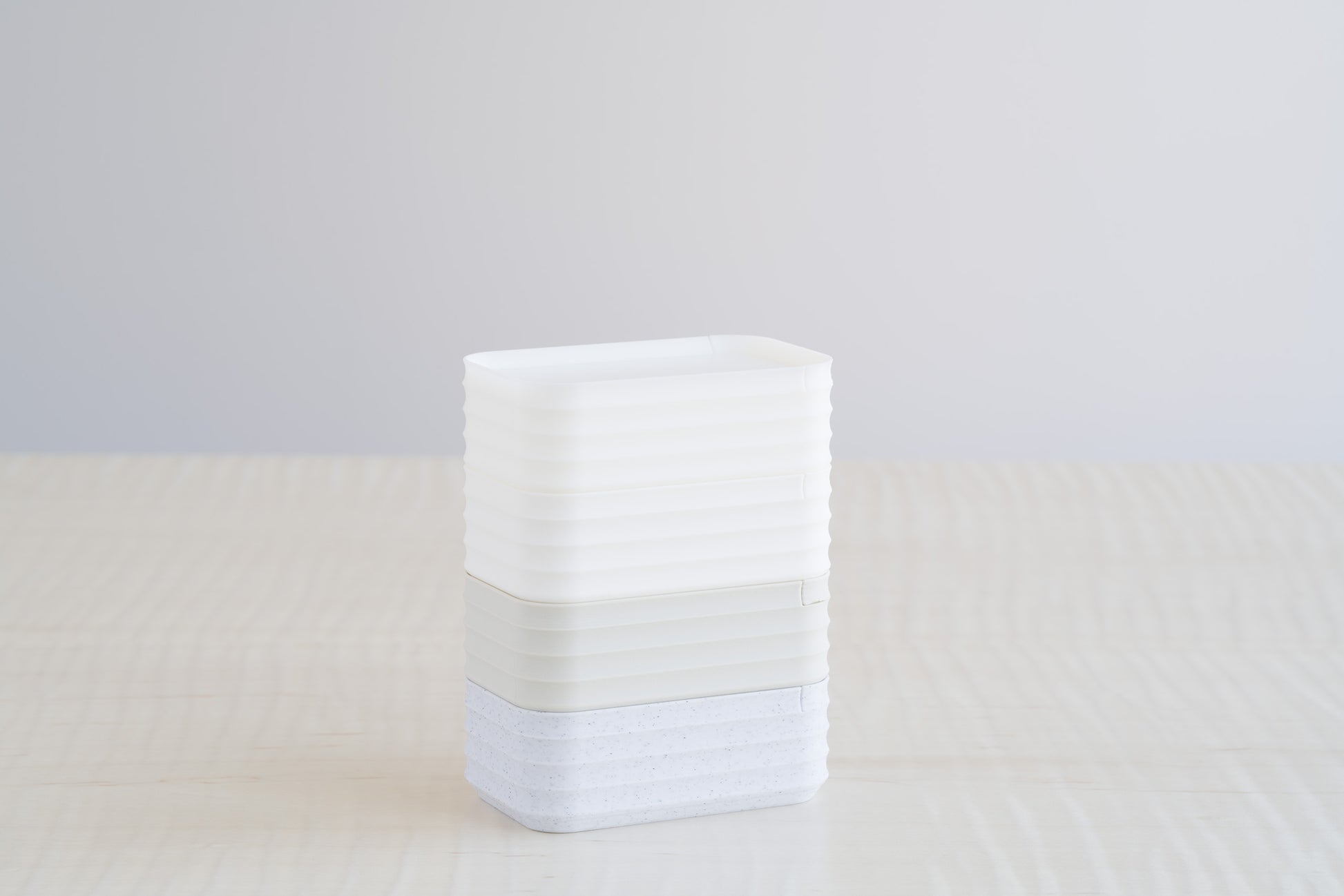 Stacked Rib Series Mini Boxes in white, matte ivory white, bone, and marble speckle finishes, arranged vertically on a light wood table.