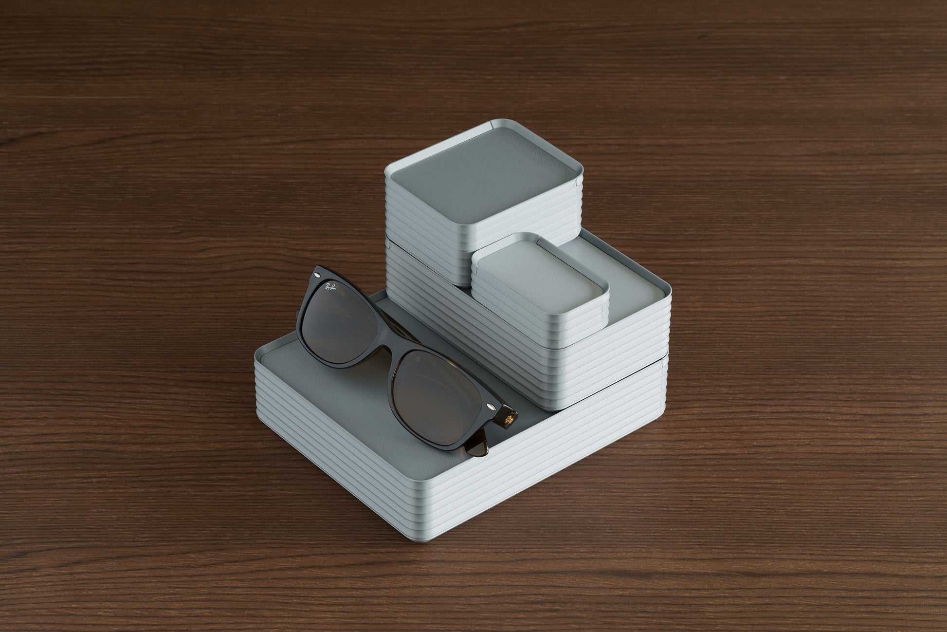 Arrangement of four silver Z Co boxes on walnut surface with sunglasses for scale
